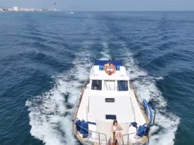 A woman relaxes on the deck of a yacht as it cruises through beautiful blue waters, showcasing the perfect blend of leisure and scenic views.