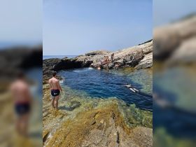 A lively group enjoys a sunny day swimming in clear waters by a rocky beach, perfect for summer adventures and outdoor fun.