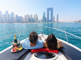 A couple relaxes on a boat with a fruit platter and champagne, enjoying stunning views of the city skyline — a perfect setting for a romantic getaway or celebration.