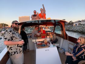 A lively group enjoys a sunset boat party, sharing drinks and laughter aboard a beautifully crafted vessel — perfect for celebrations and gatherings on the water.