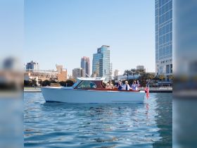 A lively group waves from a charming boat against a stunning city skyline, capturing the essence of a fun day on the water.