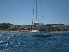 A sailboat navigates the clear waters near a picturesque coastline, with guests enjoying the scenic views — an ideal setting for a sailing adventure.