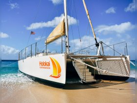 A stunning view of the Holokai catamaran docked on a sandy beach, showcasing its sleek design and vibrant colors against a clear blue sky.