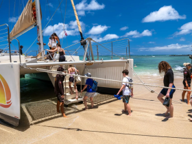 A lively group boards a catamaran from the beach, ready for an exciting day on the water — perfect for adventure seekers and beach lovers.