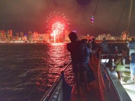 Guests aboard a boat enjoy a spectacular fireworks display against the backdrop of a vibrant city skyline, creating a memorable celebration on the water.