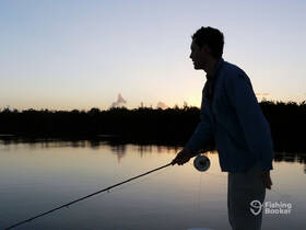 A fisherman casts his line at sunset, creating a stunning silhouette against the tranquil waters — a perfect moment for fishing enthusiasts.