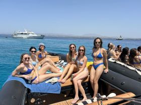A lively group of friends enjoys a sunny day on the water, relaxing on a boat in bikinis — perfect for summer parties and celebrations.
