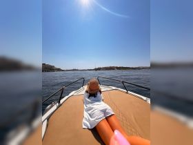 A woman relaxes on the bow of a boat under the sun, enjoying a serene day on the water — perfect for sunbathing and leisure activities.