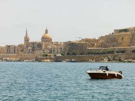 A scenic view of a boat cruising near the historic coastline of Malta, showcasing the stunning architecture and vibrant waters — perfect for exploring the beauty of the Mediterranean.