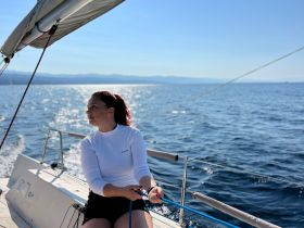 A woman enjoys a sunny day sailing on the ocean, actively engaging with the boat's rigging — a perfect moment for sailing enthusiasts.