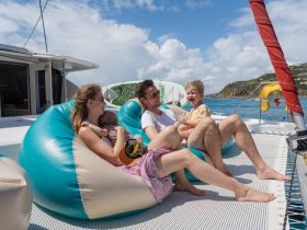 A joyful family enjoys quality time on a catamaran, relaxing on bean bags with stunning ocean views — perfect for memorable family adventures on the water.