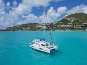A stunning aerial view of a catamaran named 'Mojito' sailing through vibrant turquoise waters, with lush hills in the background — perfect for tropical adventures.