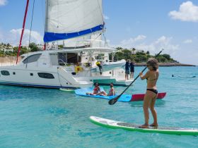 A lively scene featuring a group enjoying paddleboarding and relaxing on a catamaran, showcasing the perfect beach day filled with fun and water activities.