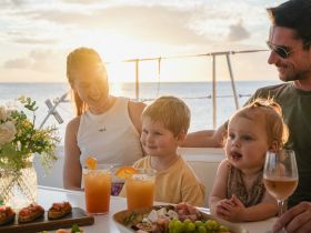 A joyful family enjoys a sunset dining experience on a boat, complete with cocktails and delicious appetizers — perfect for memorable moments on the water.