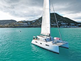 A stunning aerial view of a catamaran sailing through turquoise waters, set against a backdrop of lush hills and coastal homes, perfect for exploring beautiful destinations.