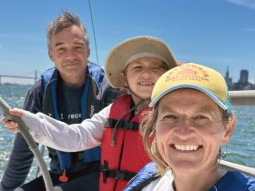 A joyful family enjoys a sailing adventure on the water, capturing smiles against a scenic backdrop of the city skyline.