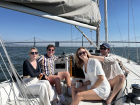 A group of friends enjoys a sunny day sailing, capturing moments of joy against the backdrop of the Bay Bridge — perfect for memorable outings on the water.