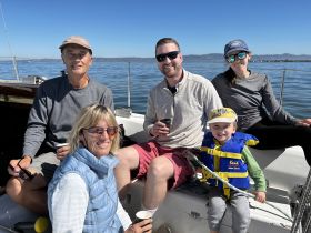 A joyful family enjoys a sailing trip together, capturing a moment of fun and relaxation on the water. The child is safely wearing a life jacket, highlighting a family-friendly boating experience.