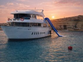 A stunning view of the 'Blue Star' yacht at sunset, showcasing its elegant design and a waterslide, perfect for luxurious outings on the water.
