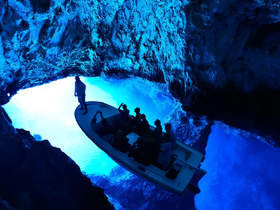 A group of adventurers explores a stunning blue cave aboard a small boat, capturing the magical interplay of light and water — an unforgettable experience in nature.