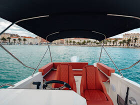 A stylish interior view of a boat's helm and seating area, showcasing comfortable red upholstery against a backdrop of scenic waterfront architecture.