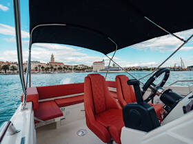 A stylish interior view of a boat's helm and seating area, showcasing comfortable red upholstery and a scenic waterfront backdrop.
