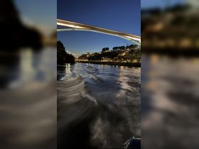 A serene night view of a waterway illuminated by city lights, showcasing a bridge and the gentle ripples of the water — perfect for evening boat tours.