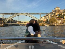 A couple shares a romantic moment on a boat with a stunning bridge backdrop at sunset, perfect for memorable celebrations on the water.