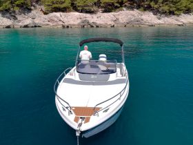A sleek speedboat is anchored in crystal-clear waters, with a lone captain at the helm, showcasing the perfect setting for a day on the water.