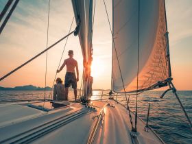 A couple enjoys a romantic sunset sail on a yacht, capturing the serene beauty of the ocean and the perfect moment for a getaway.