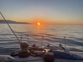 A serene sunset view from the deck of a sailboat, showcasing calm waters and distant mountains — perfect for tranquil evening cruises.