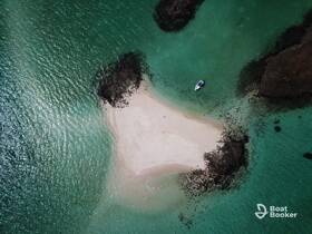 Aerial view of a small boat anchored near a secluded sandy island surrounded by turquoise waters, perfect for exploring hidden gems on your next boating adventure.