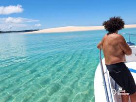 A man enjoys the stunning view from a boat, surrounded by crystal-clear waters and a sandy beach in the background — a perfect setting for a relaxing day on the water.