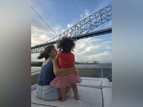 A mother and her child enjoy a scenic view from their boat, with a bridge in the background, capturing a beautiful family moment on the water.