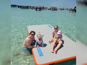 A joyful family enjoys a sunny day on a floating mat in shallow waters, creating lasting memories with their little ones — perfect for summer fun and beach outings.