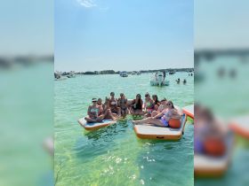 A lively group of friends enjoys a fun day on floating mats in clear waters, perfect for summer parties and relaxation under the sun.