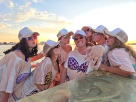 A lively group of friends celebrates a bachelorette party at sunset, showcasing fun moments and camaraderie on the water.