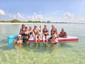 A lively group of friends enjoys a fun day in the water on floating mats, sipping drinks and soaking up the sun — the perfect summer getaway.