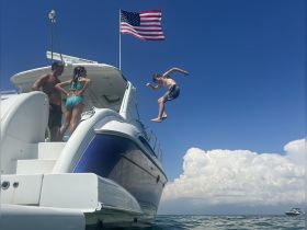 A boy joyfully jumps off the side of a boat while two adults enjoy the moment, capturing the essence of summer fun on the water.