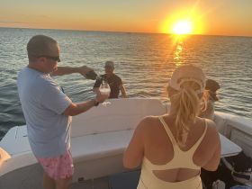 Guests celebrate at sunset aboard a boat, pouring cocktails and enjoying the scenic view — perfect for memorable gatherings on the water.