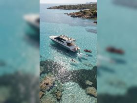A stunning aerial view of a group enjoying a day on the water, featuring a luxurious yacht and activities like swimming and paddleboarding in crystal-clear turquoise waters.