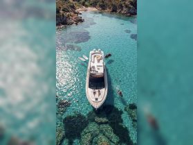 Aerial view of a luxurious yacht with a couple sunbathing on the deck, surrounded by crystal-clear waters — an idyllic setting for relaxation and adventure.