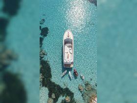 An aerial view of a luxurious yacht surrounded by clear turquoise waters, showcasing guests enjoying the sun and water activities — perfect for summer adventures.