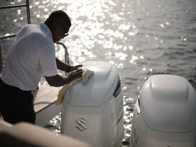 A crew member meticulously cleans the outboard motors on a boat, ensuring top performance and aesthetics for a smooth sailing experience.