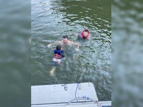 A joyful family enjoys a fun day in the water, with children wearing life jackets while swimming with an adult — perfect for summer adventures on the lake.