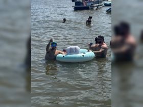 A lively group enjoys a fun day in the water, celebrating with drinks and floating mats — perfect for summer parties and relaxation.