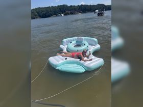 A woman enjoys a sunny day on a floating mat in the lake, perfect for relaxation and fun in the water.