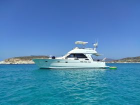 A stunning yacht anchored in crystal-clear waters, showcasing its elegant design against a picturesque backdrop of a rocky coastline.