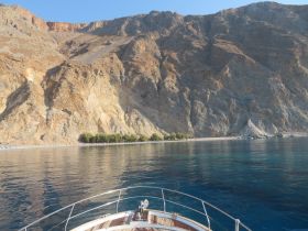 A stunning view of a serene coastline with rocky cliffs and a sandy beach, captured from the deck of a boat — perfect for showcasing beautiful destinations during a boating trip.