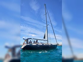 A group of friends enjoys a sailing adventure on a Jeanneau yacht, navigating through vibrant blue waters under a clear sky.